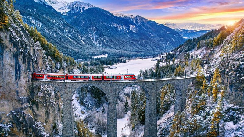 A train crossing a high level bridge in snow capped mountains in Switzerland