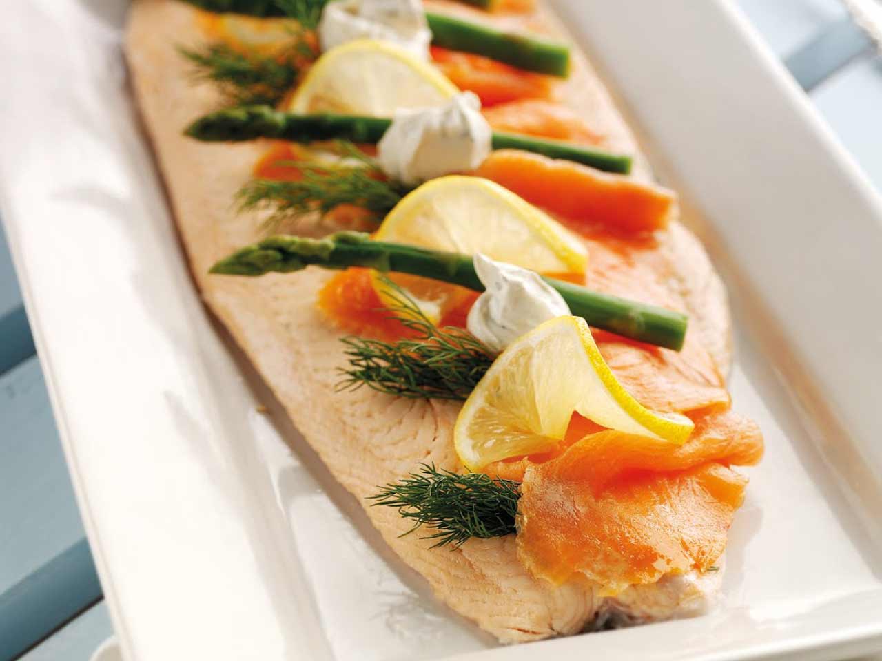 Poached salmon garnished with lemon wedges, asparagus tips and dill