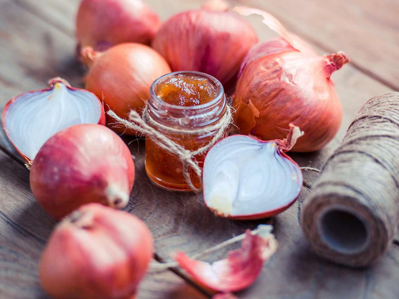 Onion marmalade surrounded by onions on wooden table