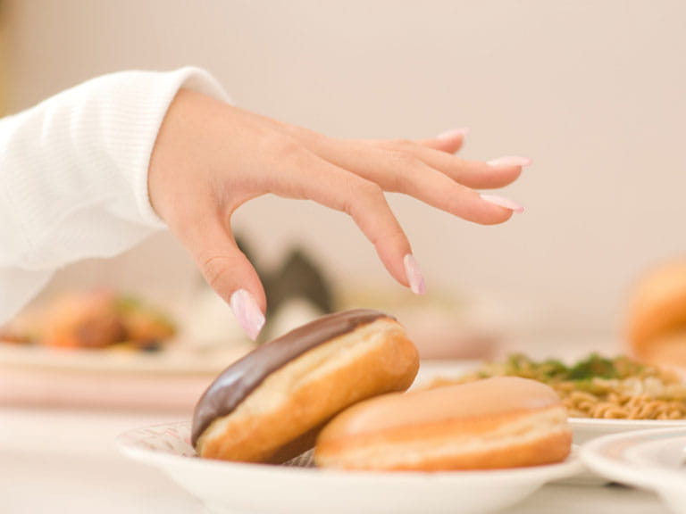 Hand reaching for a doughnut, a food high in cholesterol