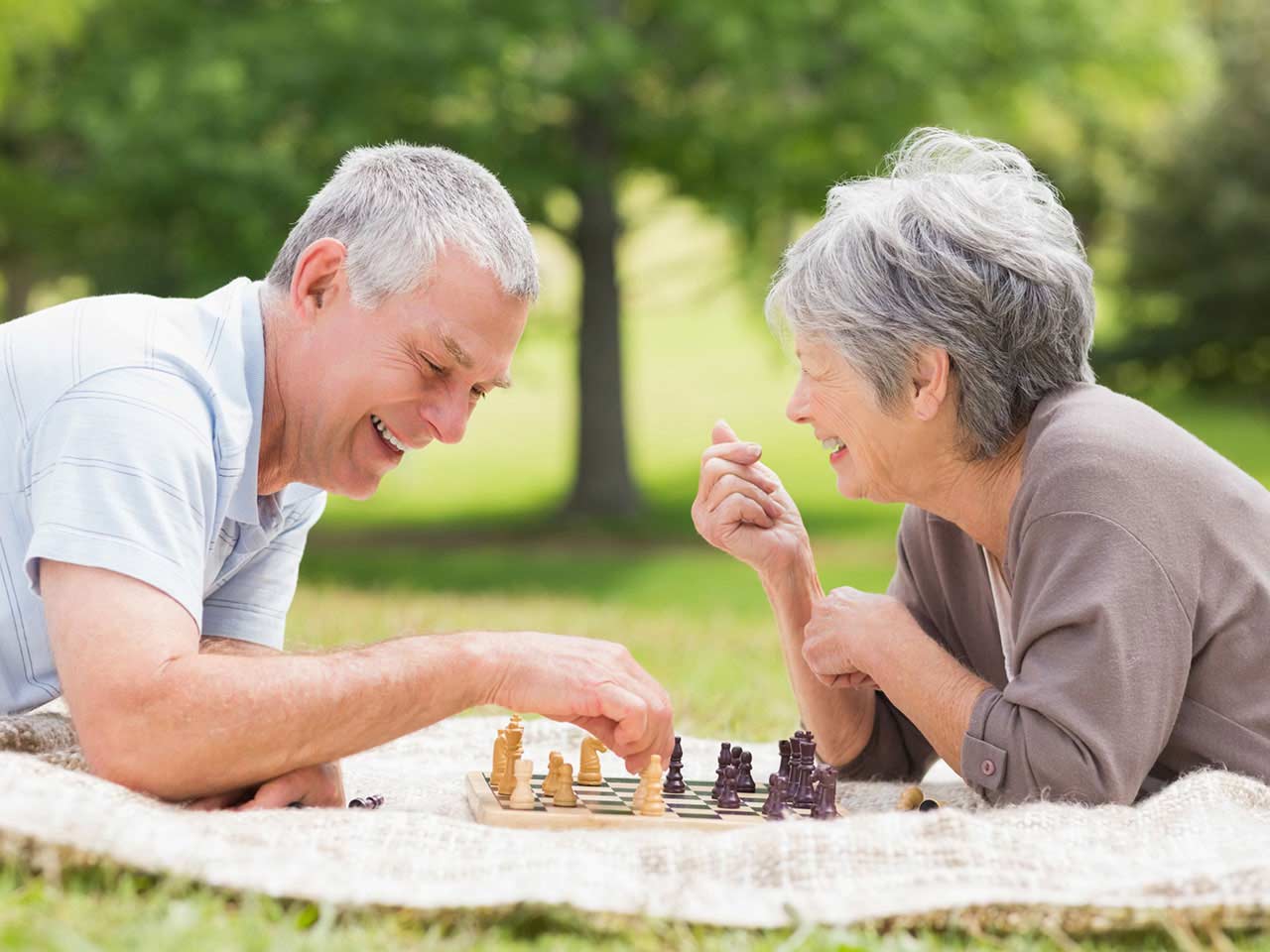 Mature couple laughing and playing chess in the park