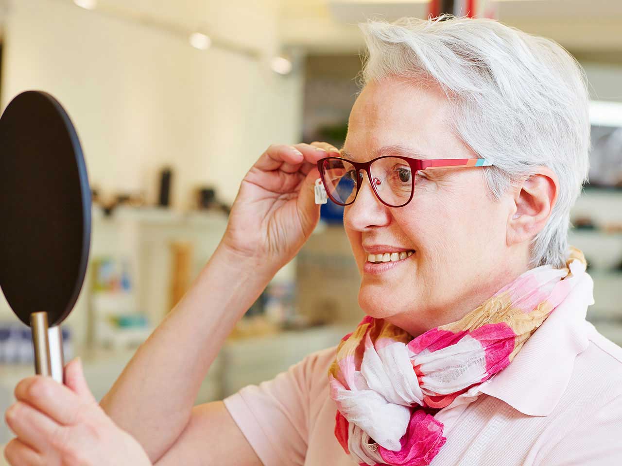 Senior lady trying on trendy glasses in opticians