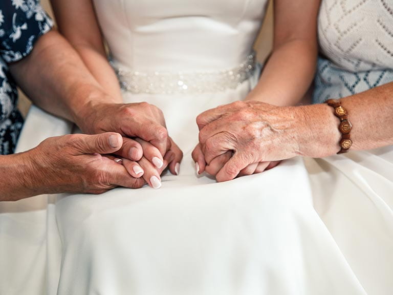 Two grandmothers hold the bride's hands on her wedding day