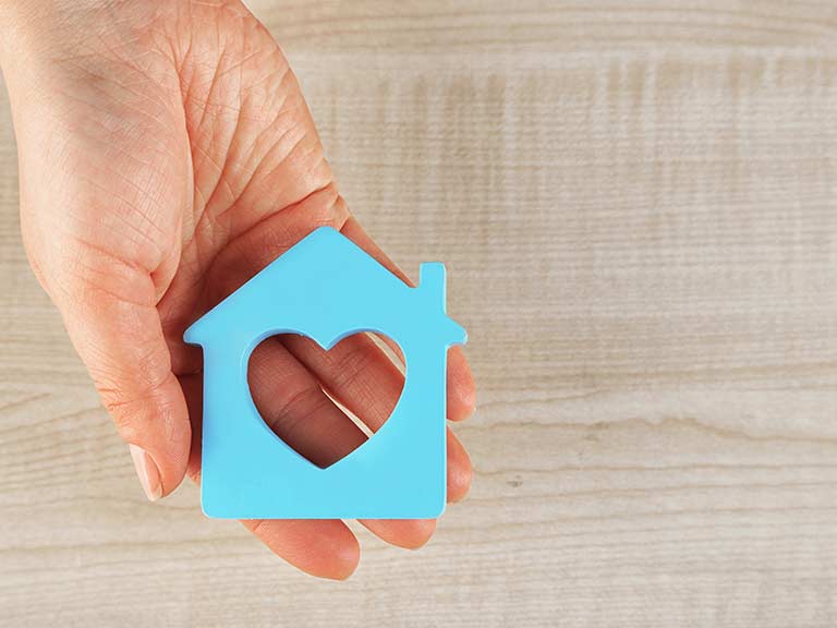 A hand holds a blue cut out of a house with a heart to represent equity release and care home fees