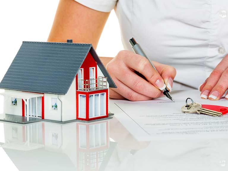 A model of a home stands next to a woman writing on an equity release form