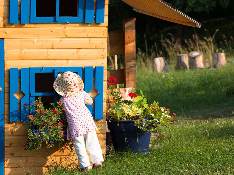 A grandchild peeks through the window of a Wendy house in the back garden