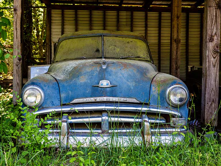 An old car slowly decays in a garden