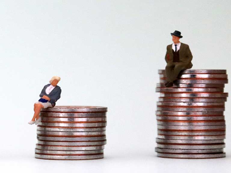 Miniature model of an oder woman sitting on small pile of coins next to a miniature model of an older man sitting on a taller pile of coins