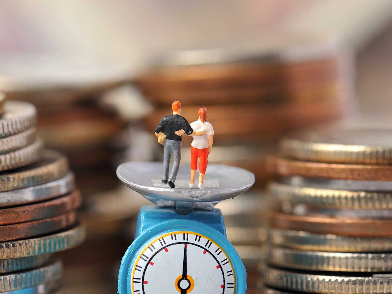 Miniature figures standing on scales surrounded by cash