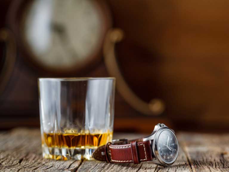 Glass of whisky with a watch beside it