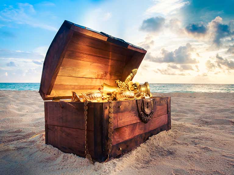 Pirate-style treasure chest on a beach, lid open and filled with gold, treasure and jewels