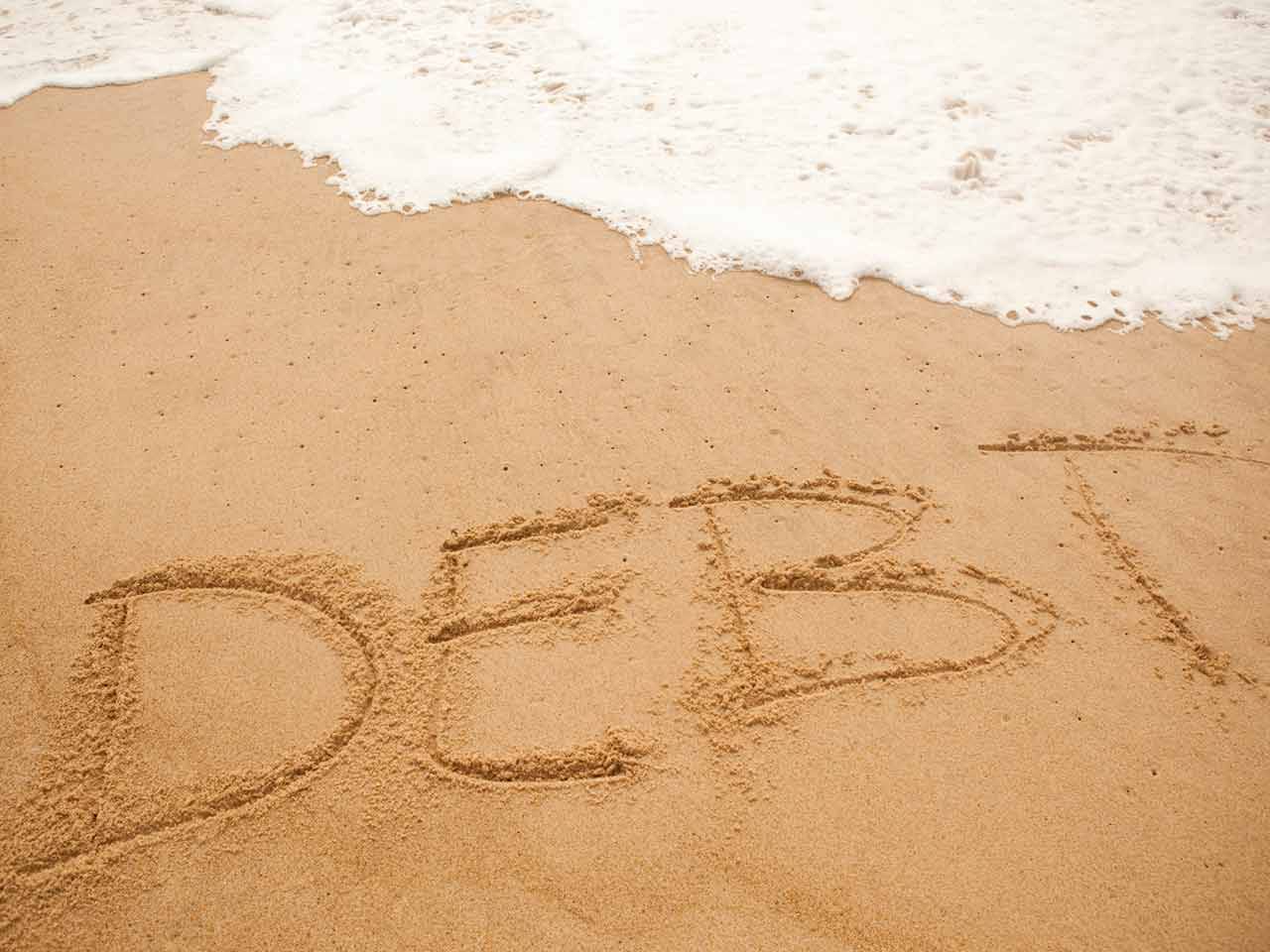 The word debt written in the sand being washed away 