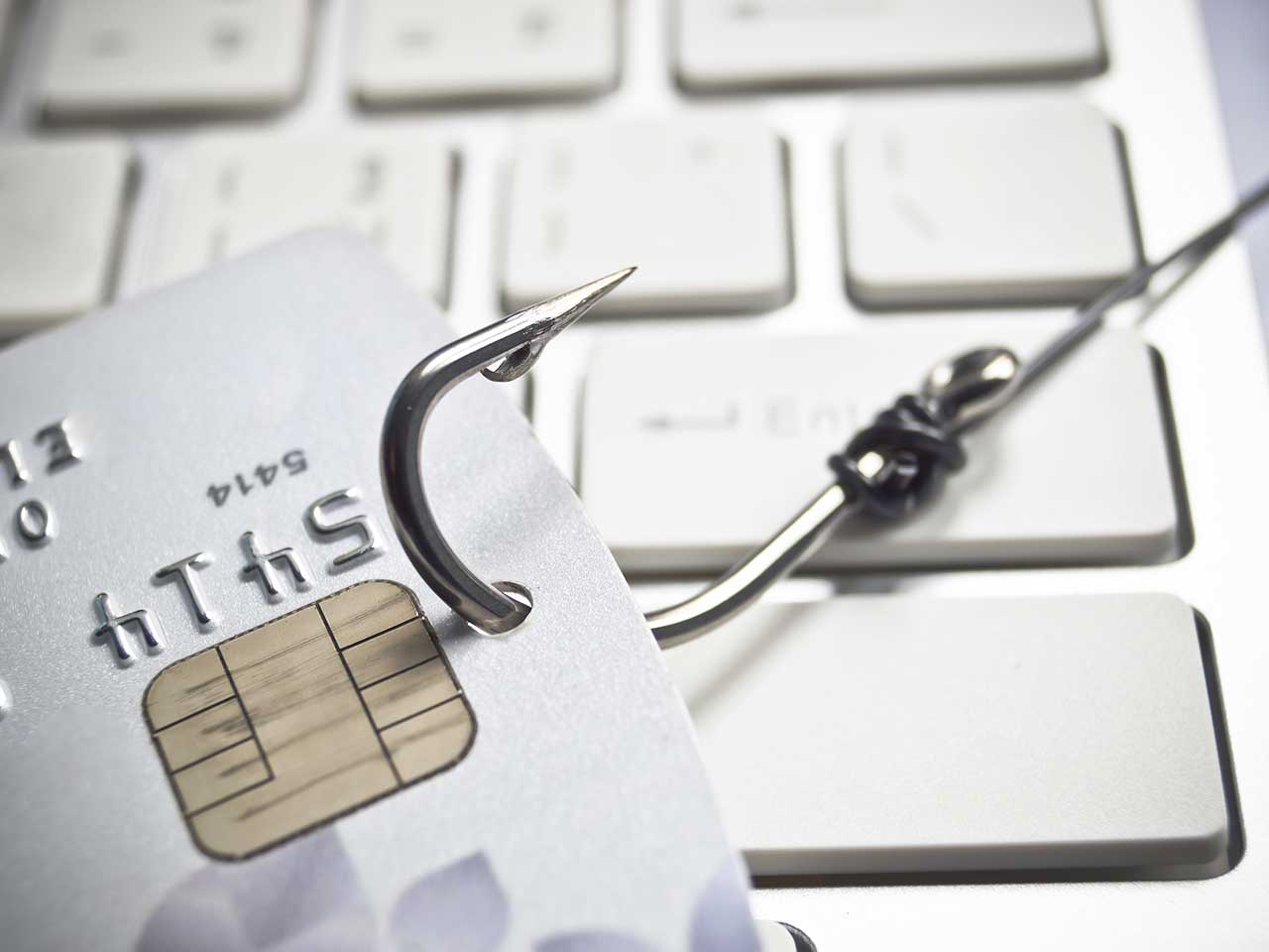 Fishing hook dragging a credit card across a computer keyboard to represent cyber crime