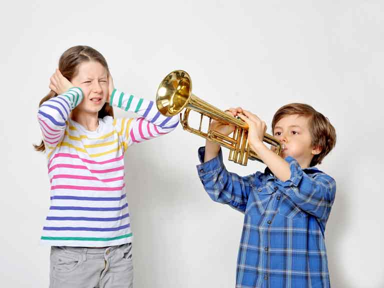 Boy playing trumpet while girl puts her hands over her ears to block out the noise
