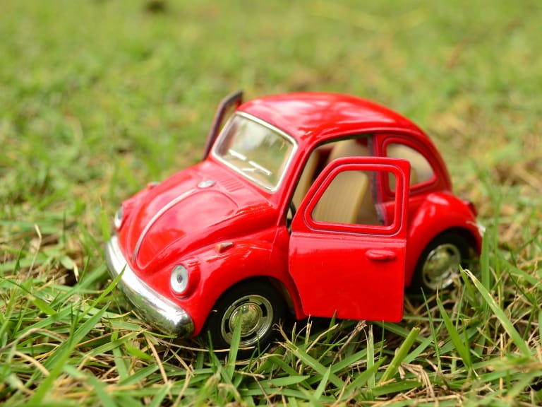 A red toy car on the grass to represent downsizing to a smaller car