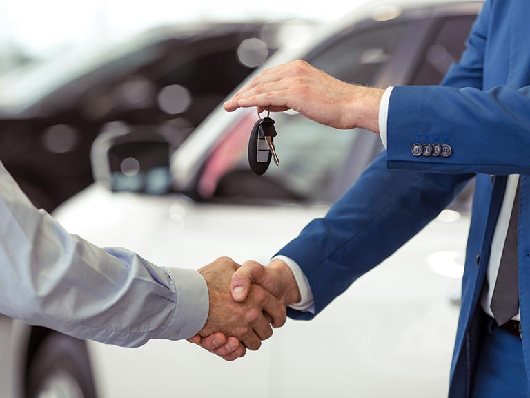Two people shake hands after selling a car