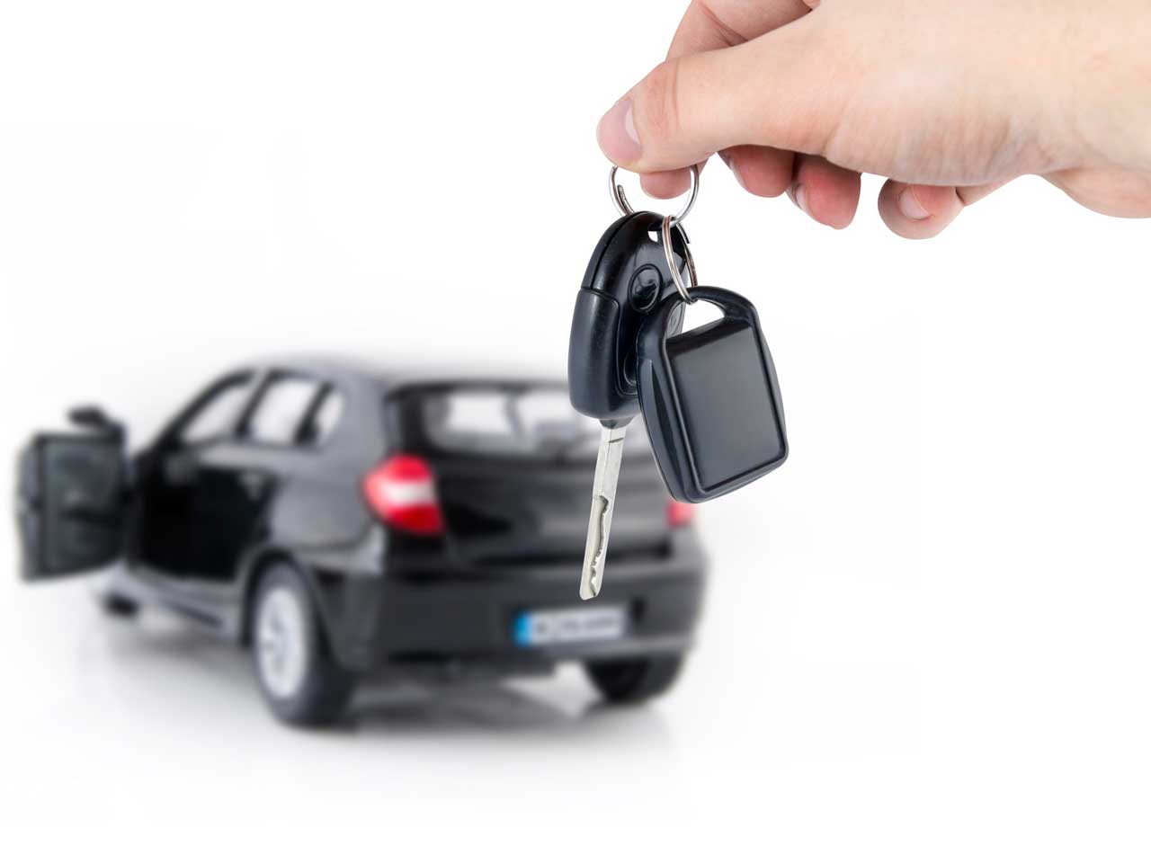 Person holding car keys in front of a car to represent buying or selling a car