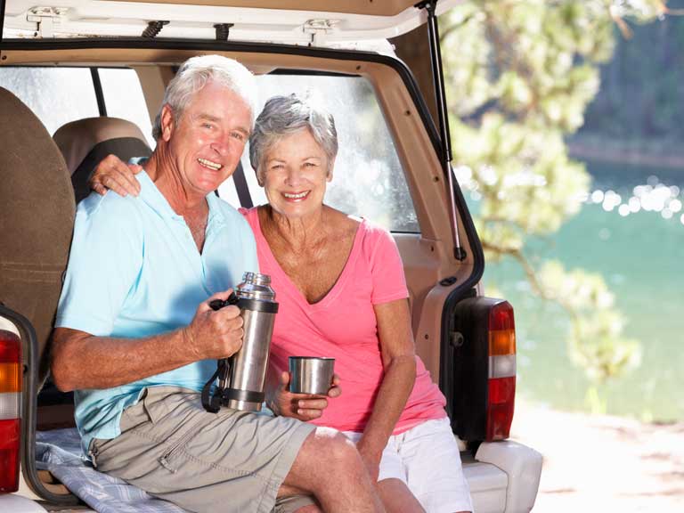 Couple drinking from a flask outside their car to represent travelling and road trips