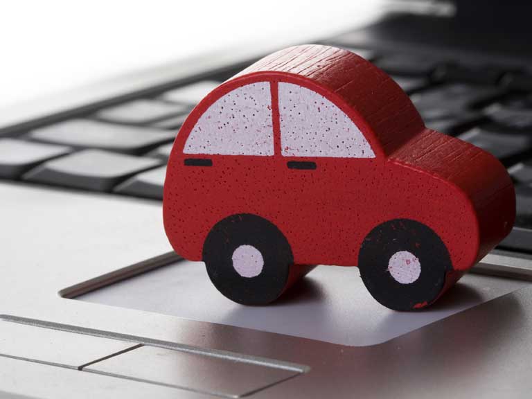 Toy car resting on a keyboard to represent selling cars online