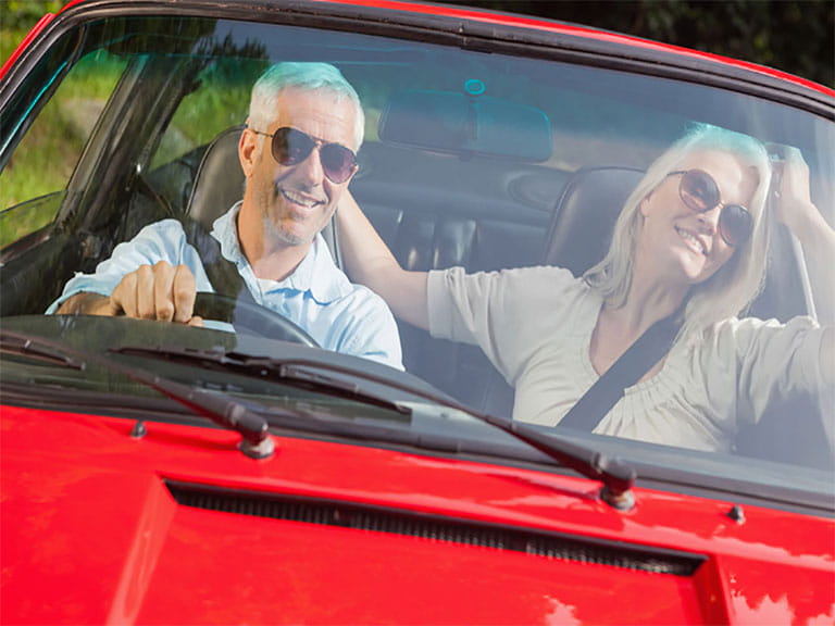 Mature couple driving a sportscar, having renewed their driving licences at 70