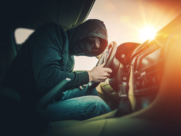 A thief breaking into a car to steal the owner's valuable items