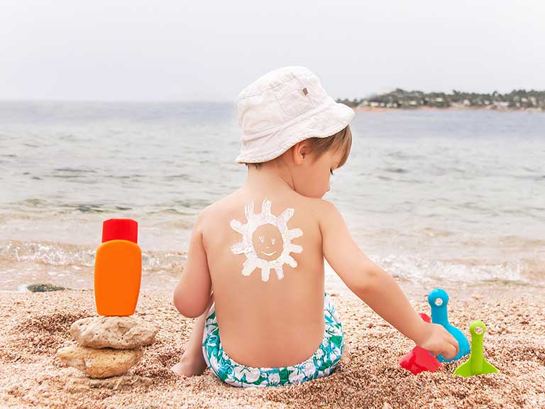 A small child sits on the beach in the sun with suntan lotion on