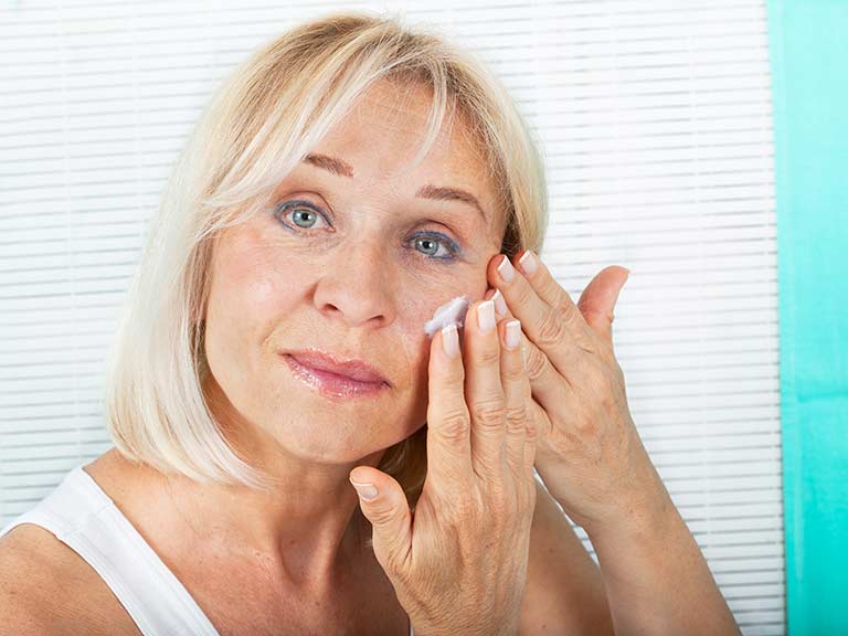 An older lady applies cream to moisturise her face