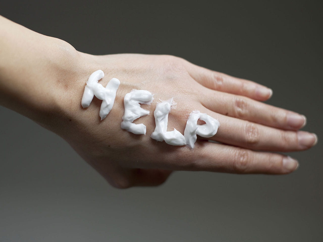 Ageing hand with help written on it in handcream
