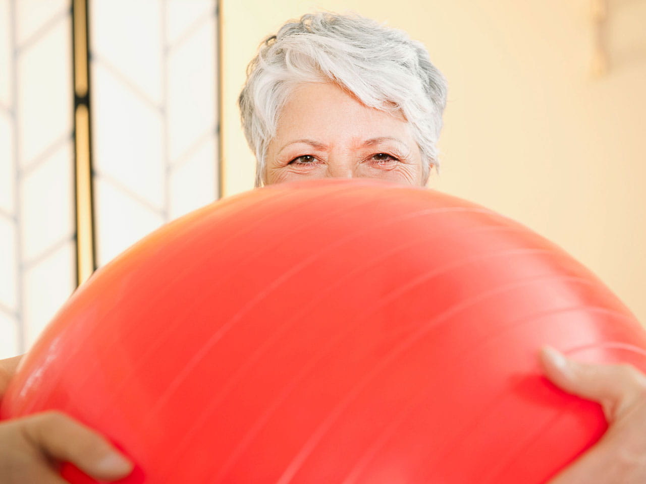 Grey haired lady holding gym ball with smiley eyes