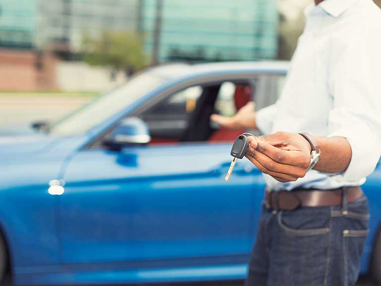 A man holds car keys and gestures to a car to represent a successful sale