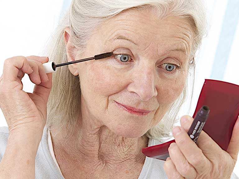 An older lady applies make-up