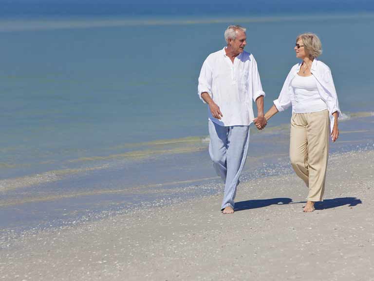 A couple walk along a beach in the sunshine - but have they applied enough sun protection for their hair?