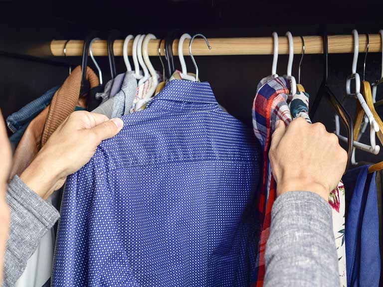 A man reaches for a tailored shirt in his wardrobe