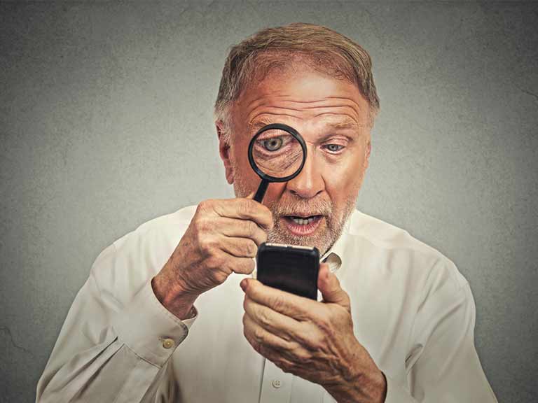 A man uses a magnifying glass to read his smartphone screen