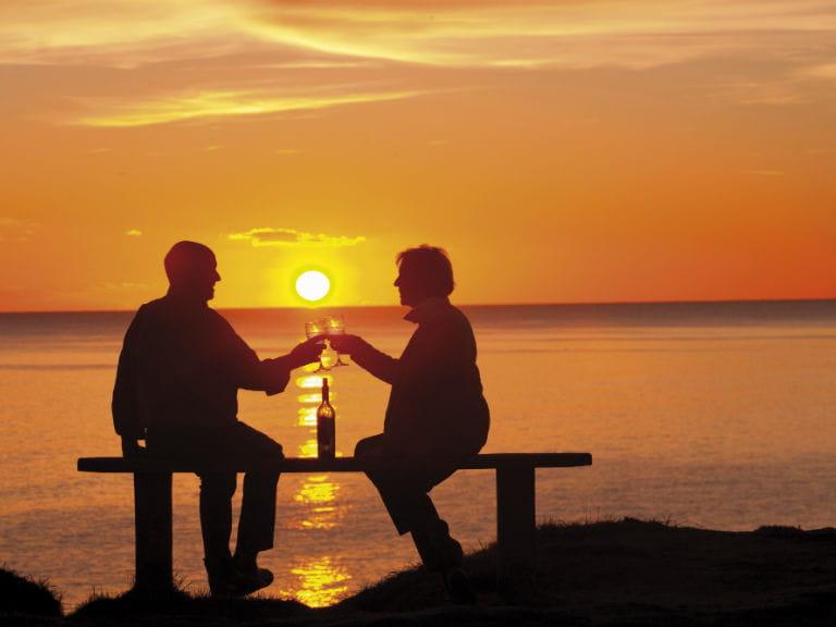 An older couple at sunset toasting against a sea backdrop