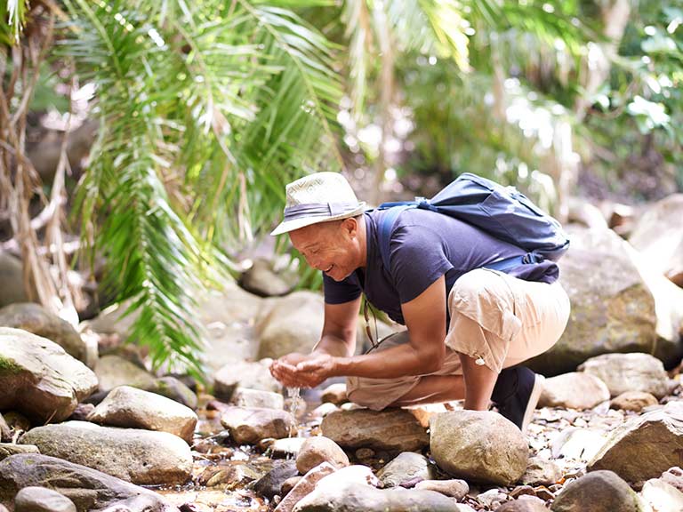 An older man drinks from a stream whilst travelling
