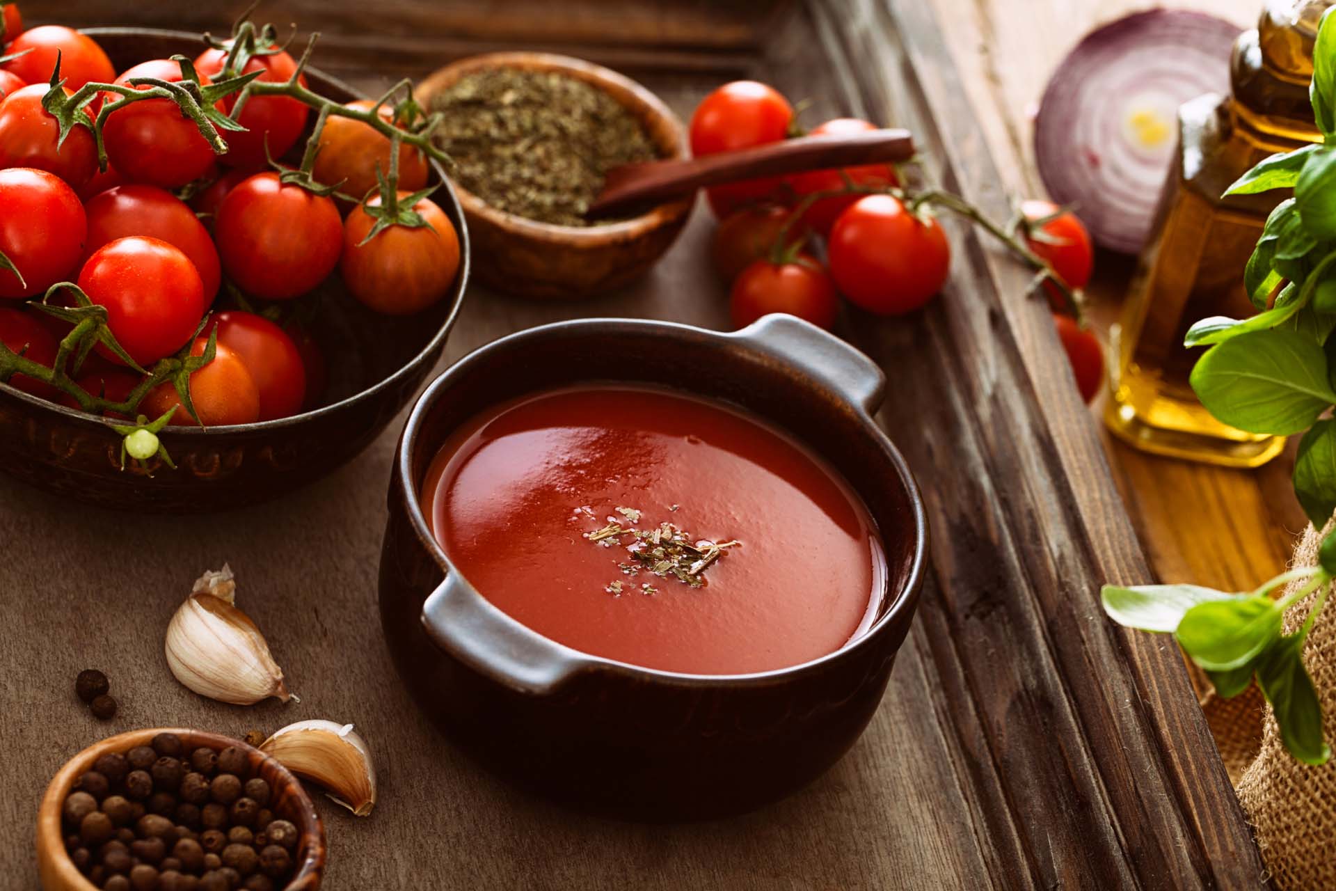 A bowl of tomato soup surrounded by fresh tomatoes on a worktop