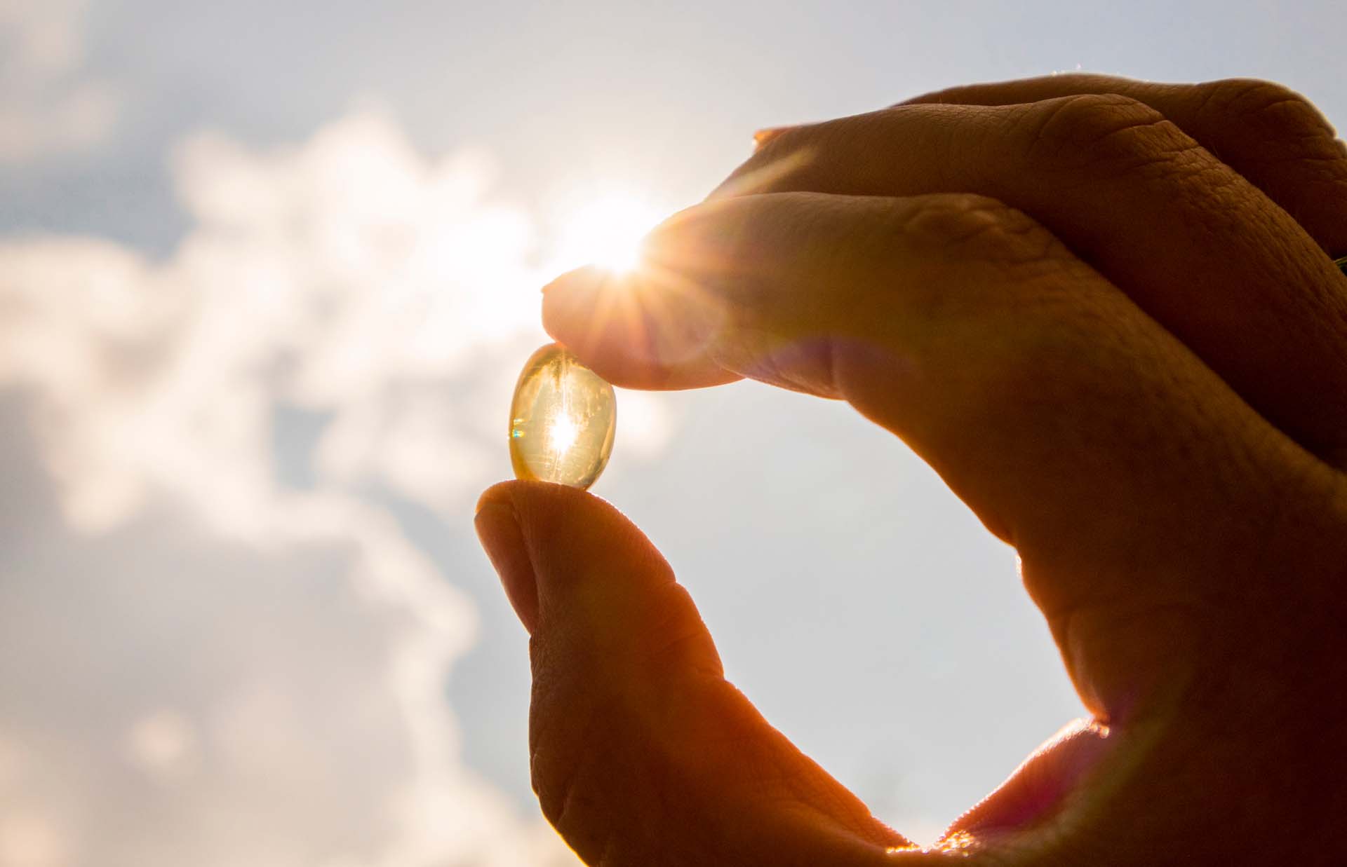 A Vitamin D capsule being held up to the sun between a man's finger and thumb