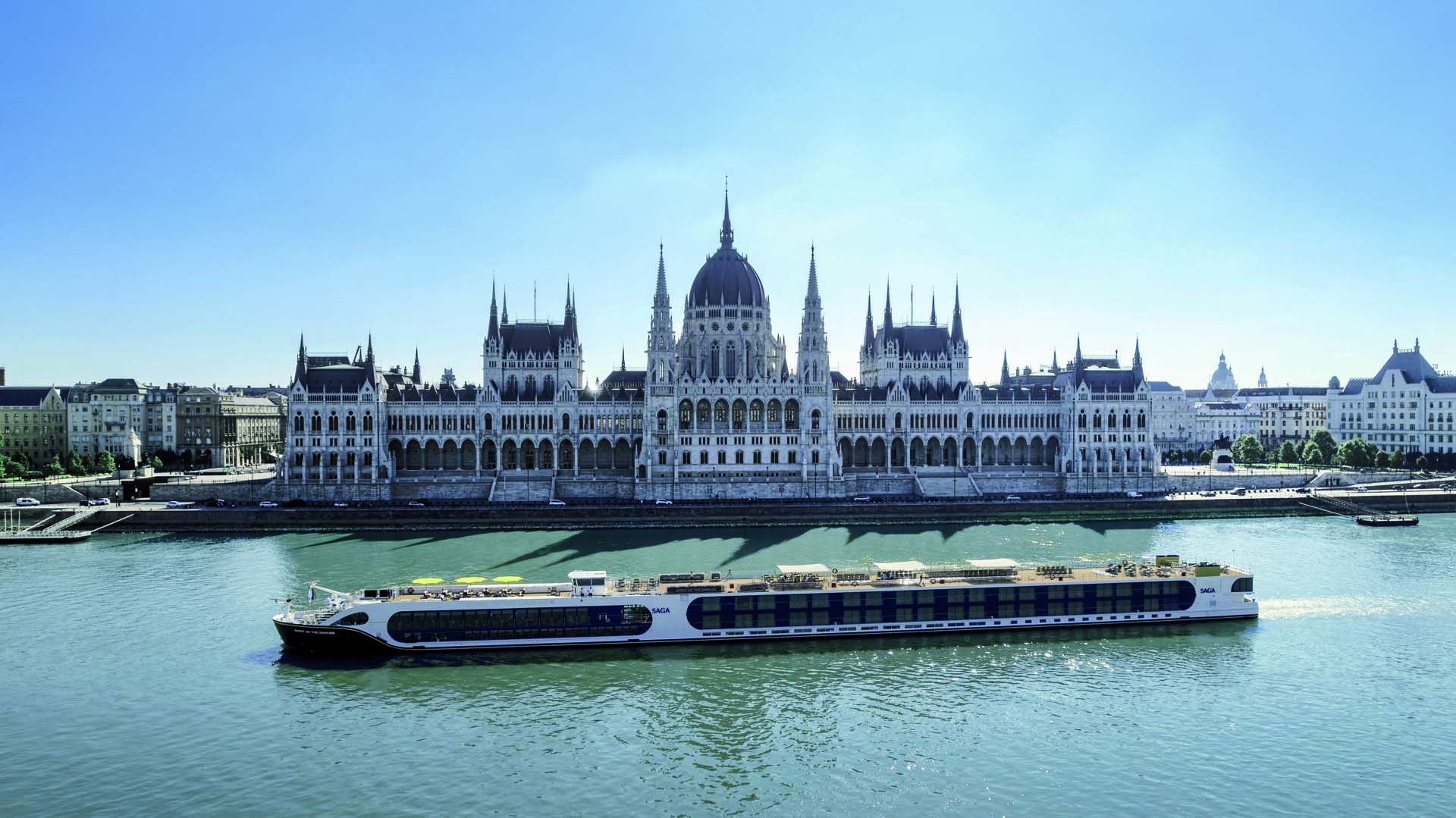 A long river cruise boat moored in front of a huge palatial building