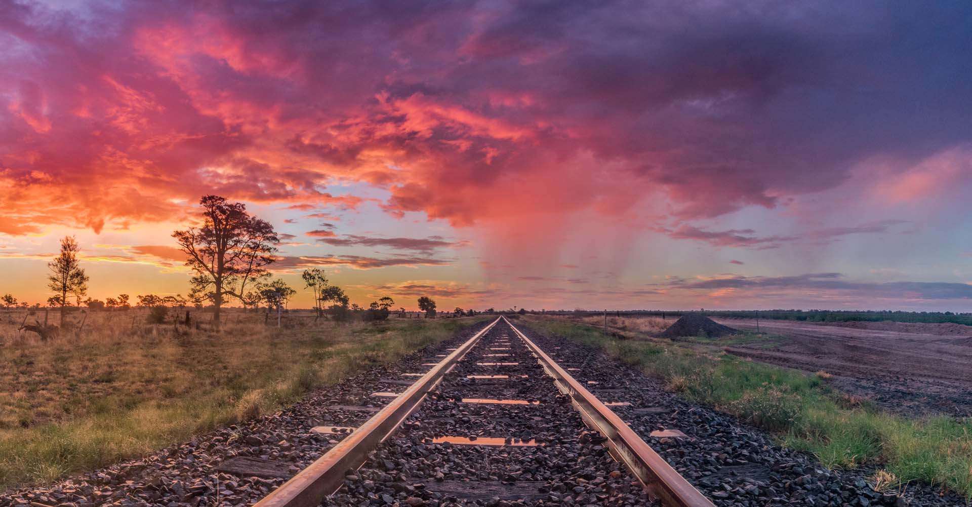 Train tracks going off into the distance across an arid landscape with a red and purple sunset.