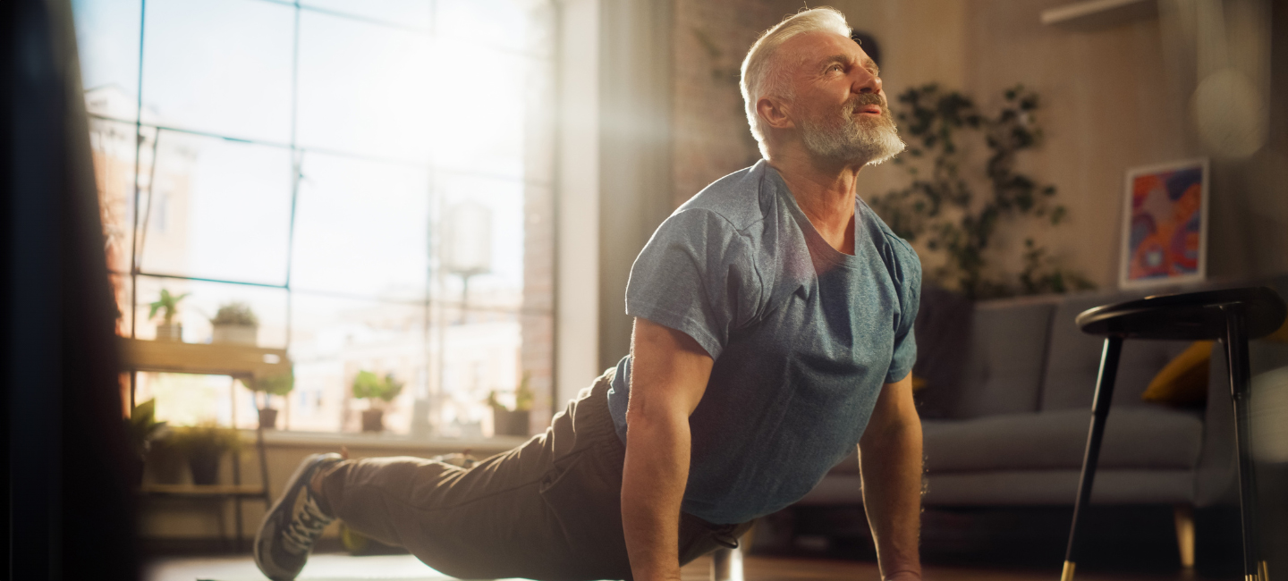 Older person in a yoga pose with sunlight streaming through the window in the background
