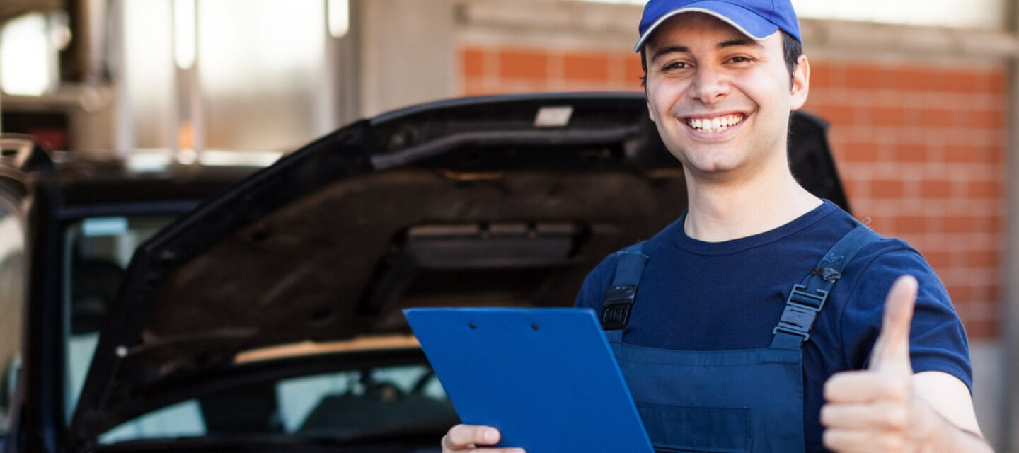 A mechanic giving a thumbs up whilst holding a clip board 