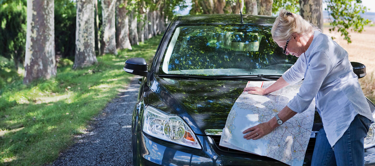A mature woman reading a map of Europe on the bonnet of her car