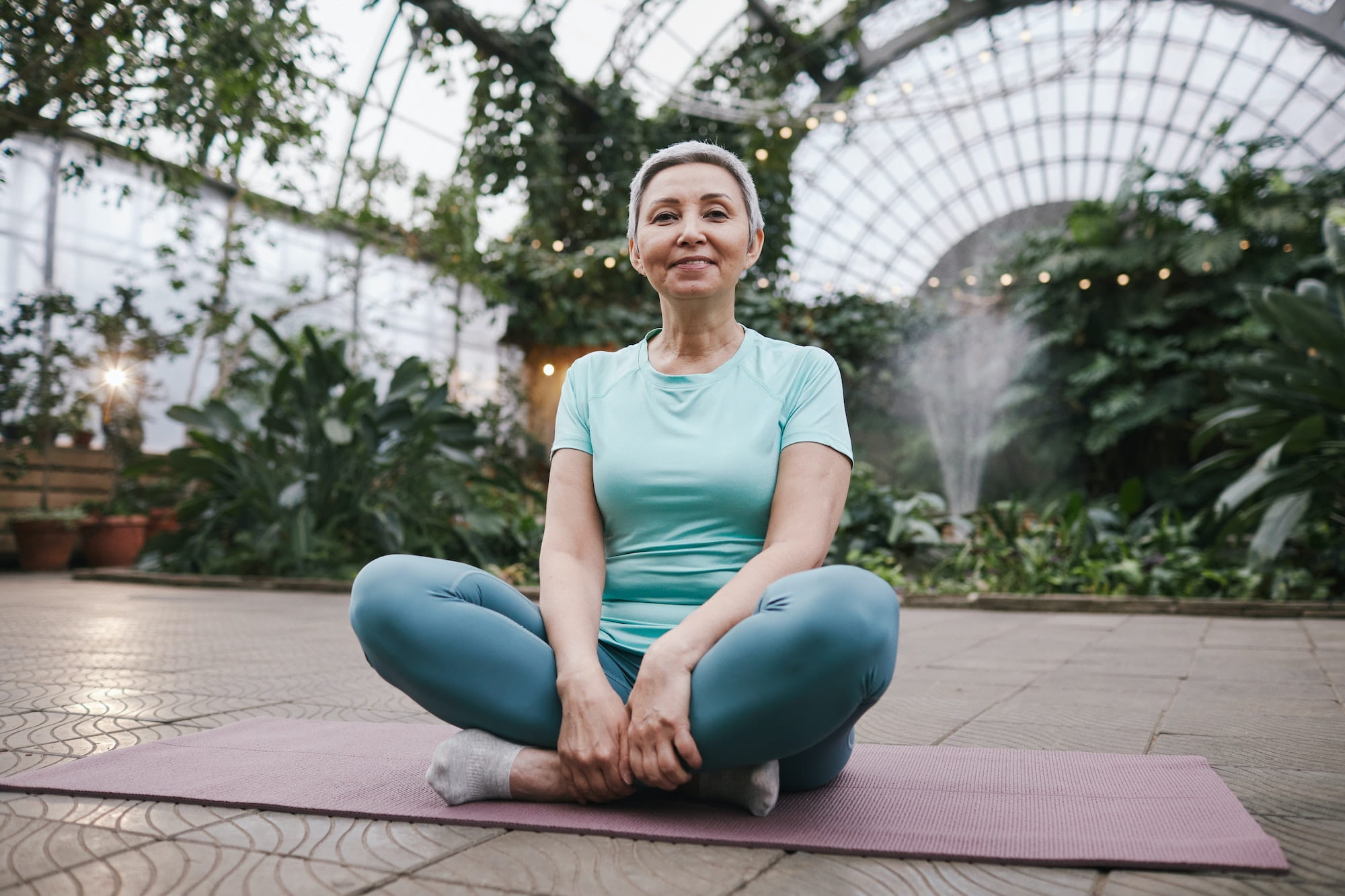 Happy woman sat on a yoga mat with plants around her