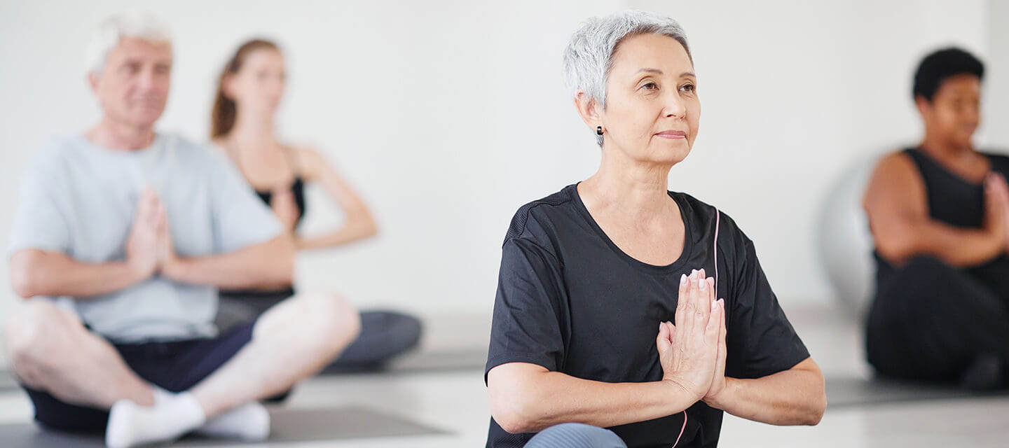 Healthy mature woman sitting on exercise mat in lotus position and doing yoga in the class
