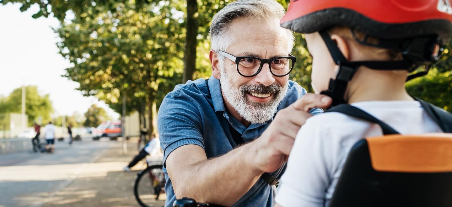 A mature man helping his grandson put his bicycle helmet on