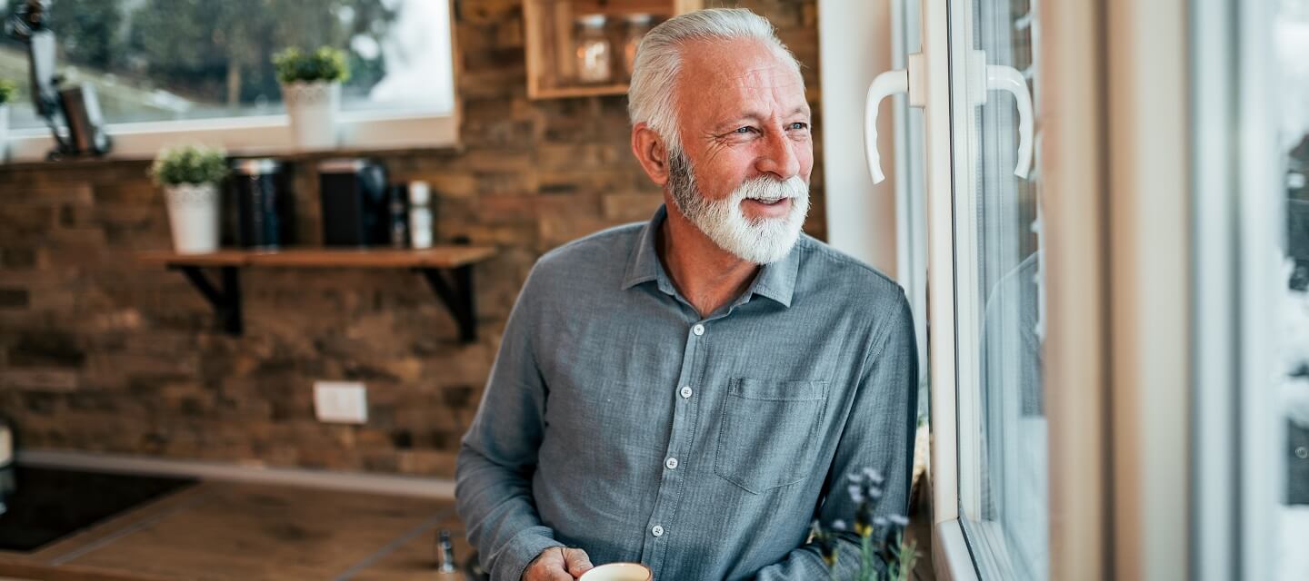 A man looking out of his kitchen window enjoying a coffee