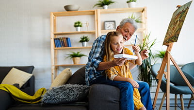 Senior man with child painting on canvas. Grandfather spending happy time with granddaughter