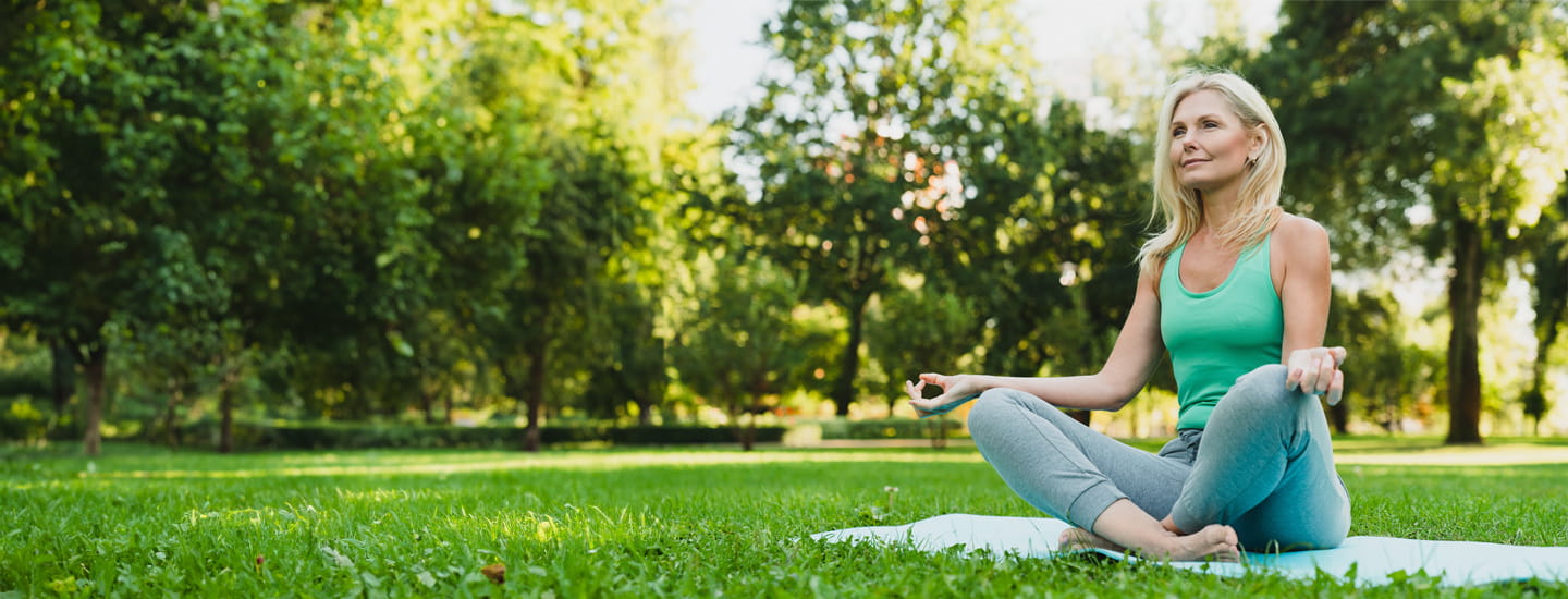 Person sitting in a cross legged yoga position on a yoga mat in a park