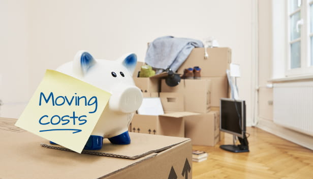 Lots of boxes and a post-it note with the words 'moving costs' stuck to a piggy bank
